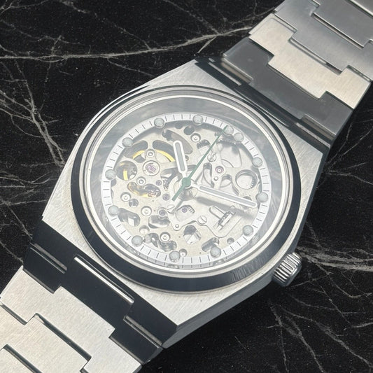 Close up of a silver mechanical watch with a detailed face on a dark marble background