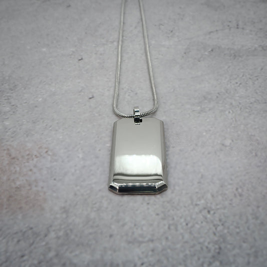 Silver rectangular pendant on a chain on a grey counter, with the chain straightened.