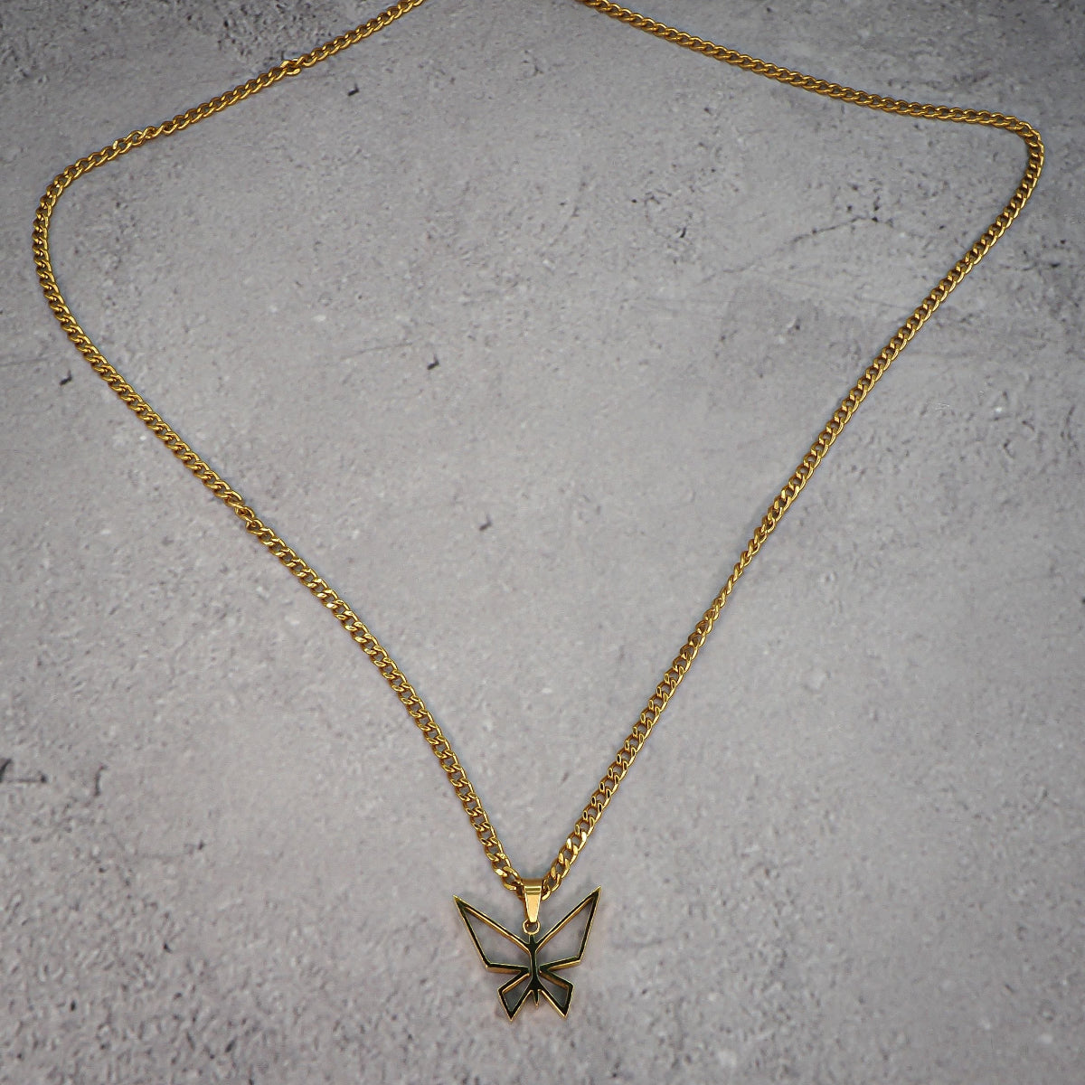 Gold necklace with a butterfly-shaped pendant on a grey counter.