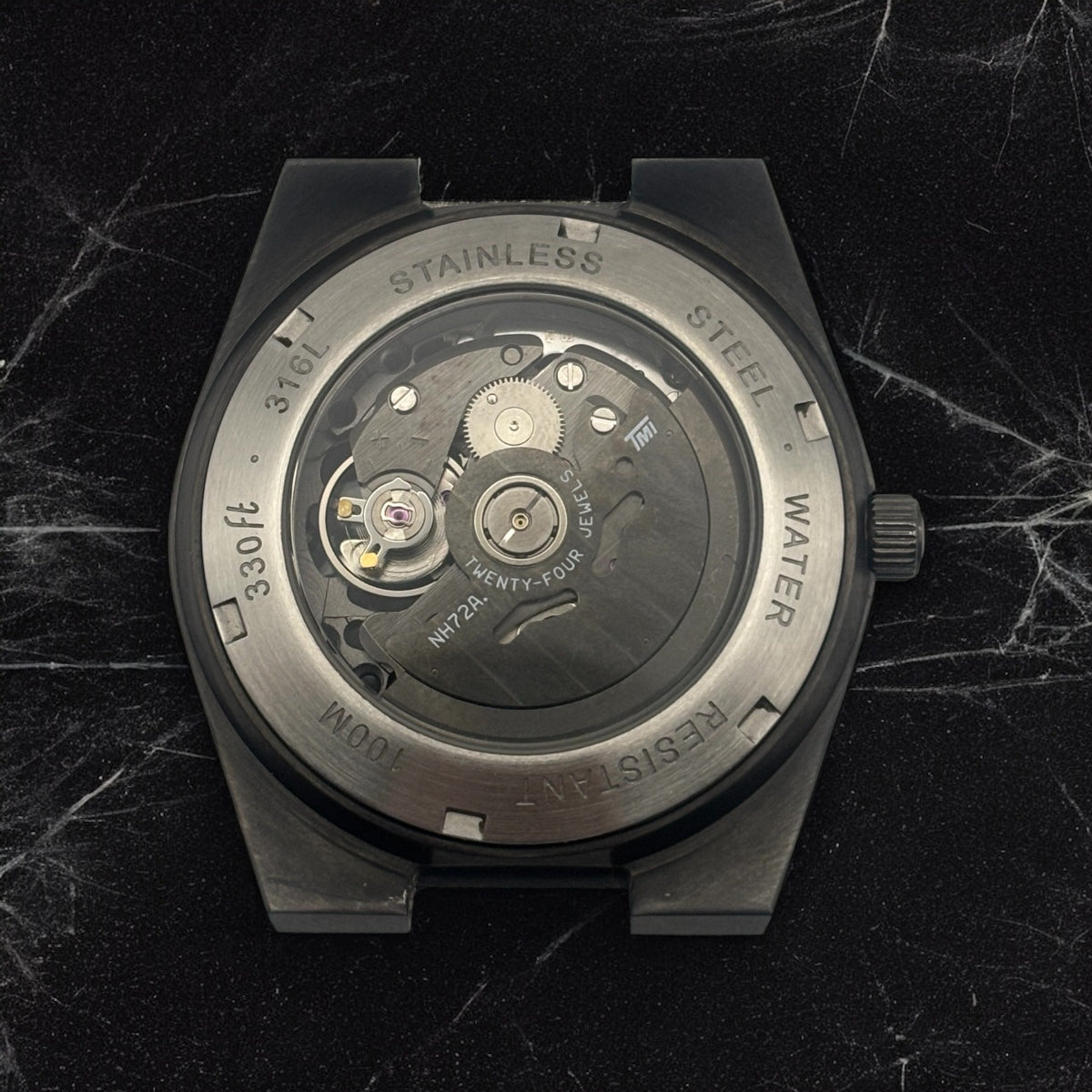 Back of the black watch with the internal mechanism visible on a marble textured surface