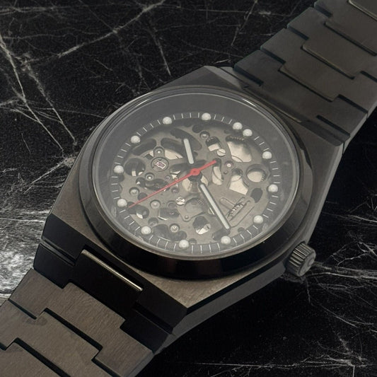Close up of a black mechanical watch with a detailed face on a dark marble background