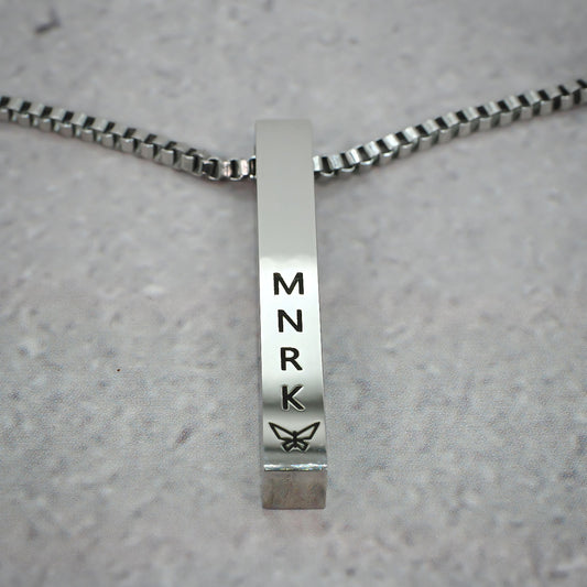 Silver bar pendant displaying 'MNRK' branding on a grey counter.