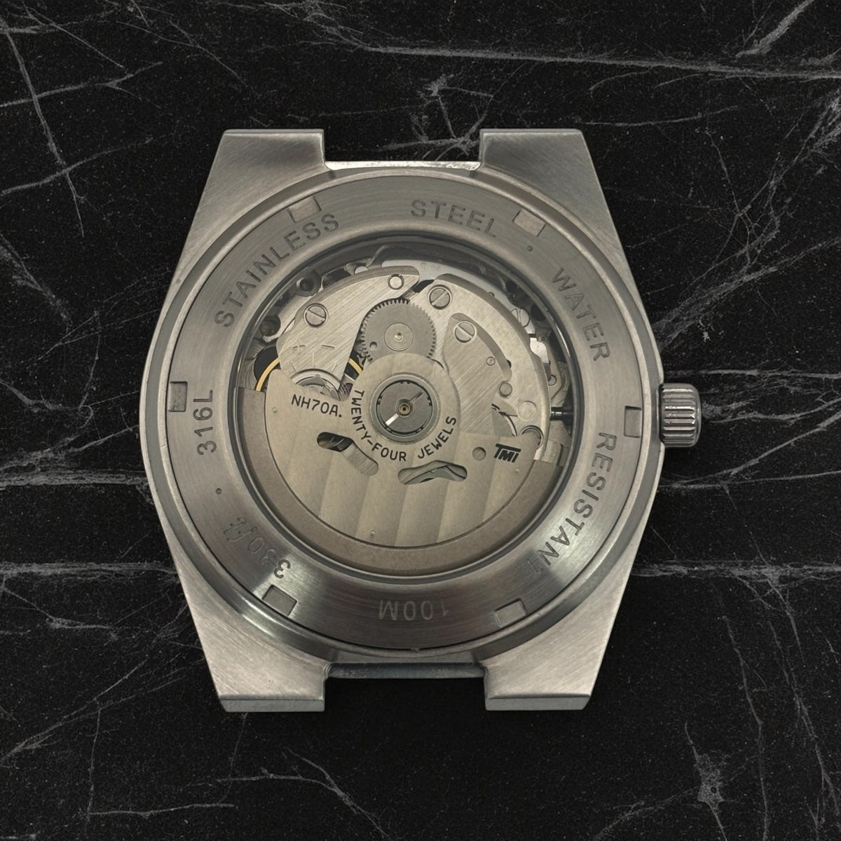 Back of the silver watch with the internal mechanism visible on a marble textured surface