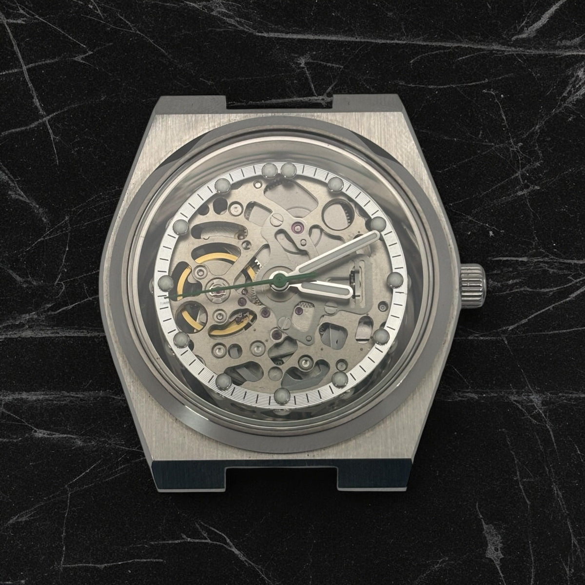 Silver mechanical watch on a dark marble background with no strap attached