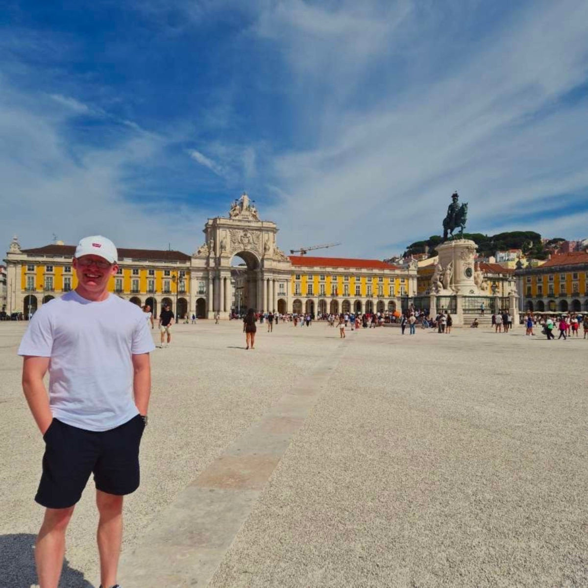 Person standing in a square with a large building and statue in the background