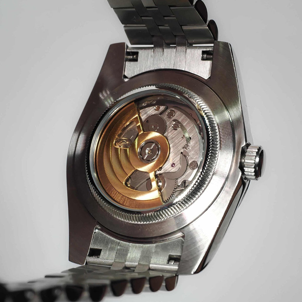 Luxury silver watch viewed from behind. A glass panel reveals the inner mechanism