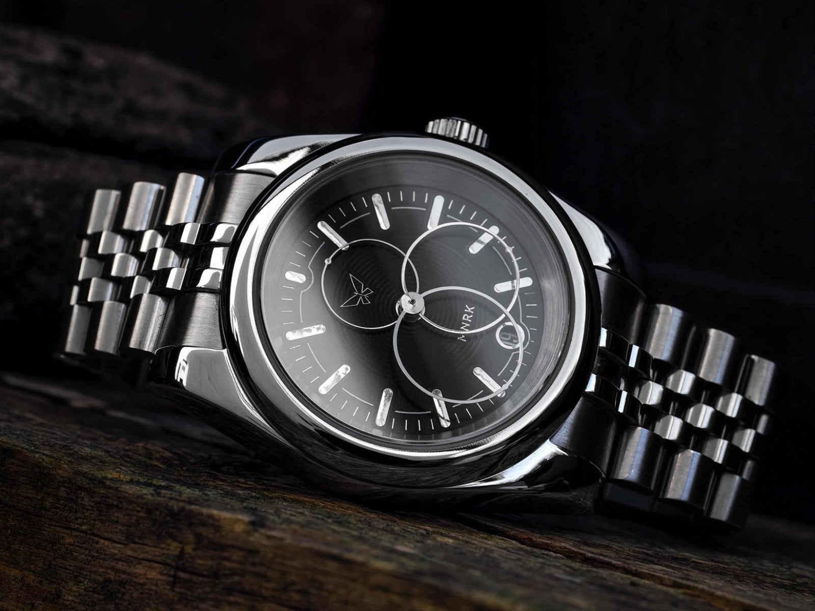 Luxury silver watch with a black dial and circular hands on a dark background, it rests on its side 
