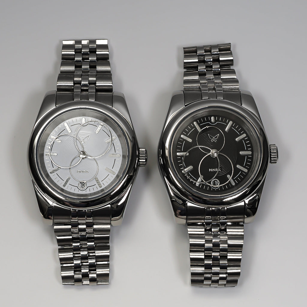 Two luxury silver watches with circular hands, one with a black dial and the other with a white one.