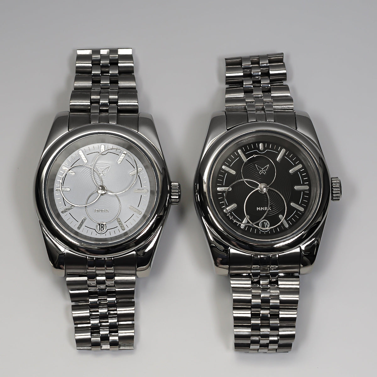 Two luxury silver watches with circular hands, one with a black dial and the other with a white one.