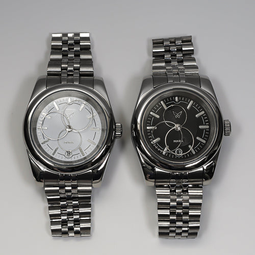 Two luxury silver watches with circular hands, one with a black dial and the other with a white one.