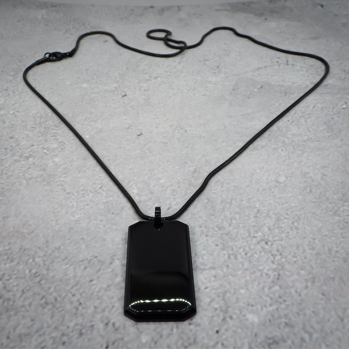 Black rectangular pendant on a chain on a grey counter.
