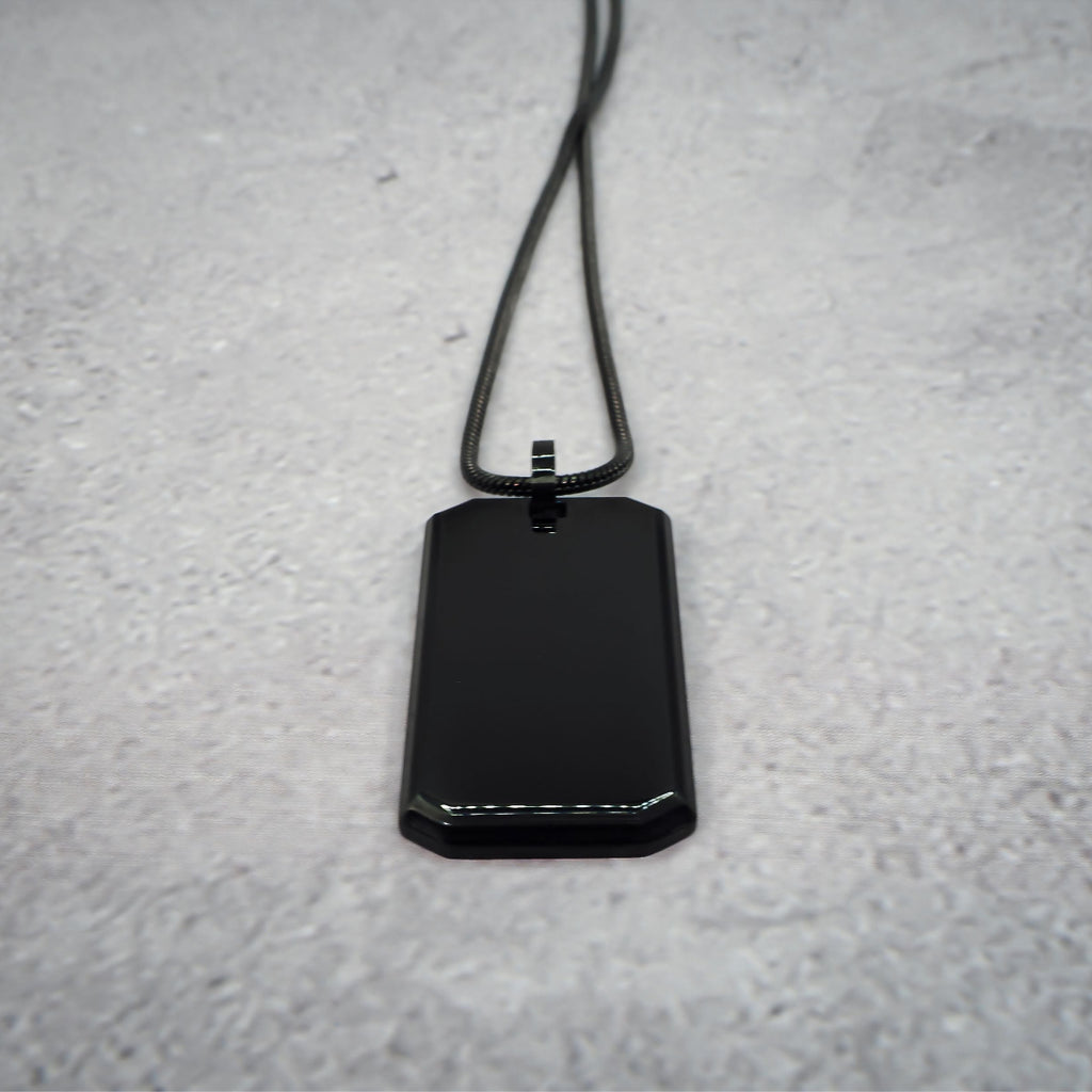 Black rectangular pendant on a chain on a grey counter, with the chain straightened.