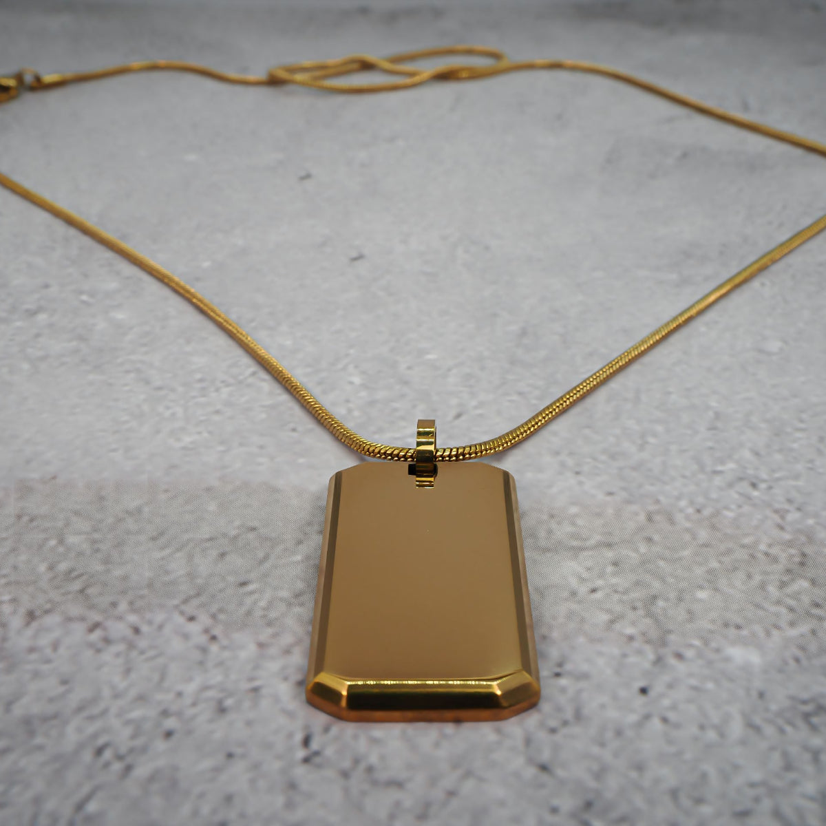 Gold rectangular pendant on a chain on a grey counter.