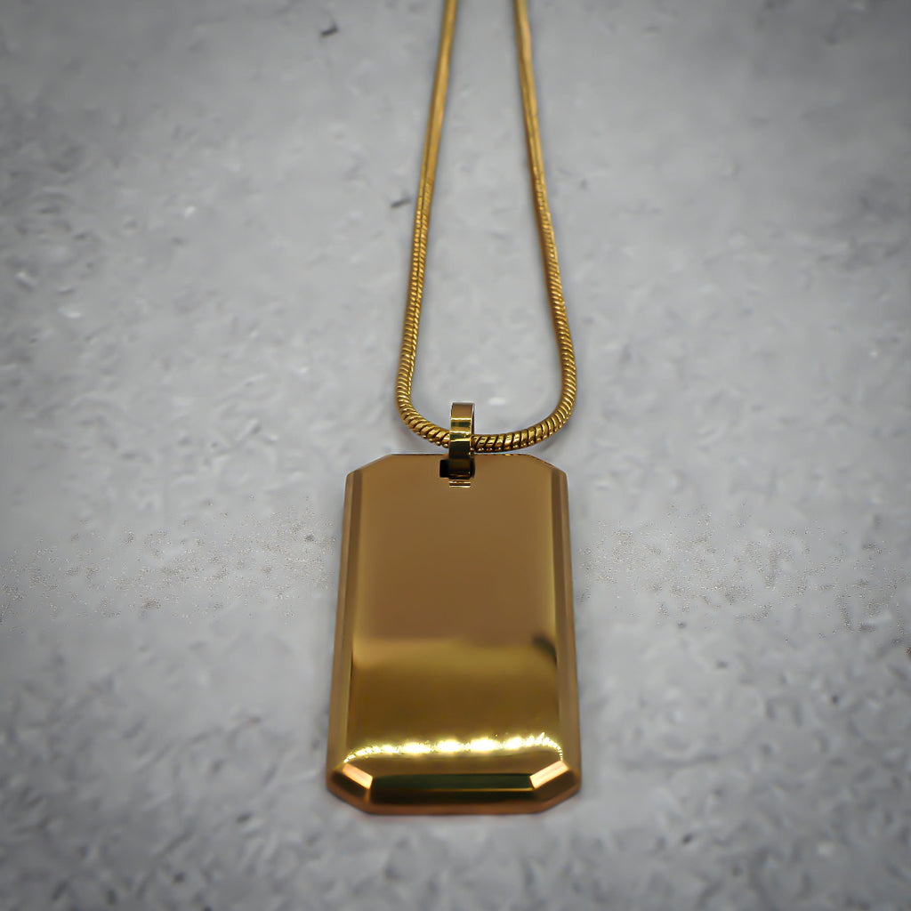 Gold rectangular pendant on a chain on a grey counter, with the chain straightened.
