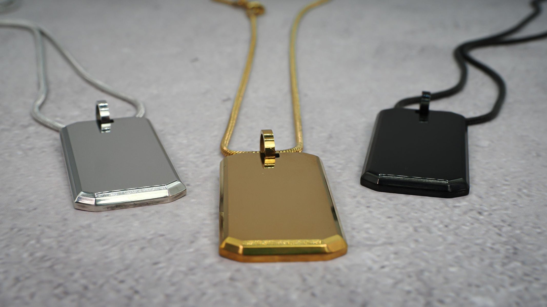 Three metallic pendants on chains, a silver one, gold one and black one