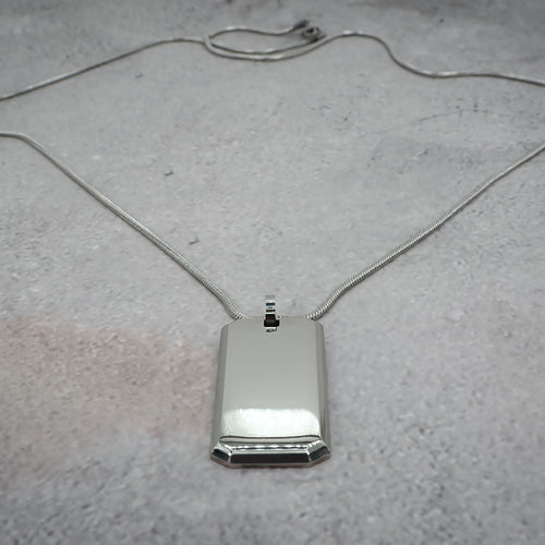 Silver rectangular pendant on a chain on a grey counter.