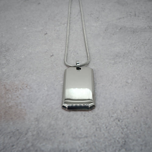 Silver rectangular pendant on a chain on a grey counter, with the chain straightened.
