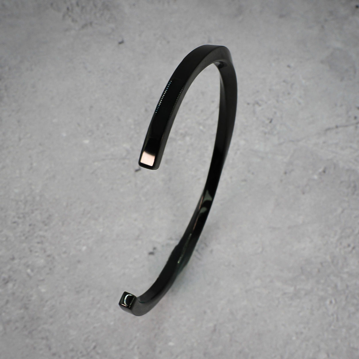 Black metal bracelet standing on its side on a grey counter.