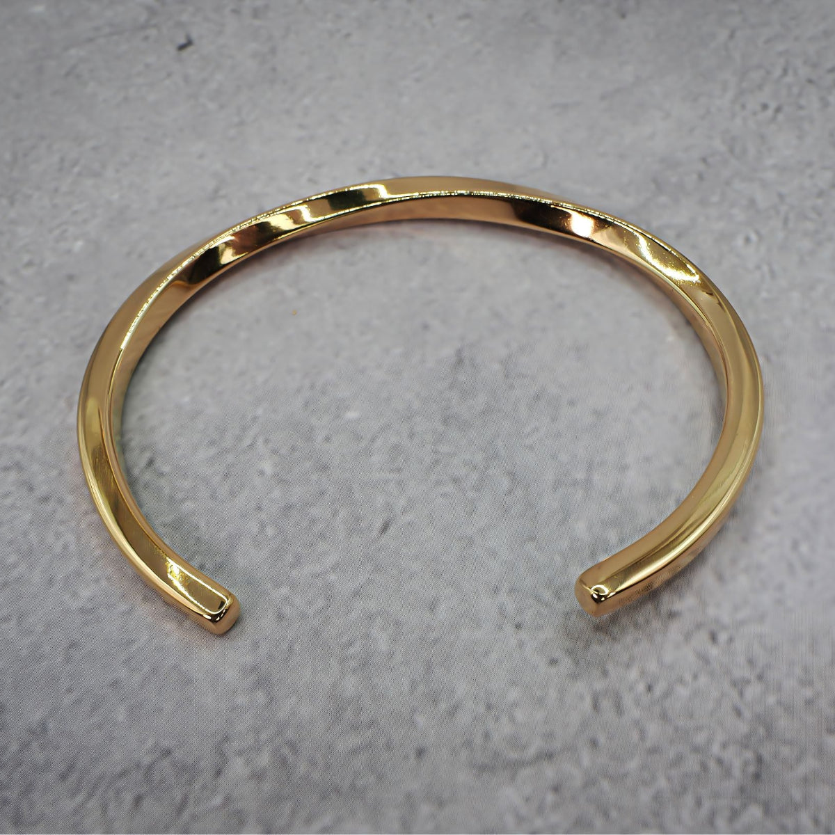 Gold metal bracelet on a grey counter.