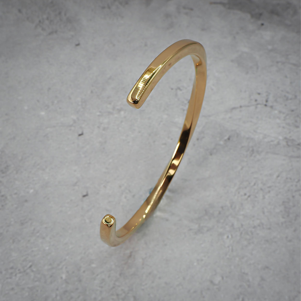 Gold metal bracelet standing on its side on a grey counter.