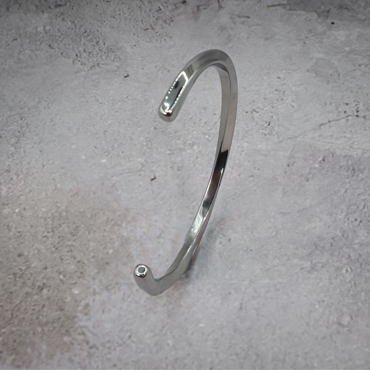 Silver metal bracelet standing on its side on a grey counter.