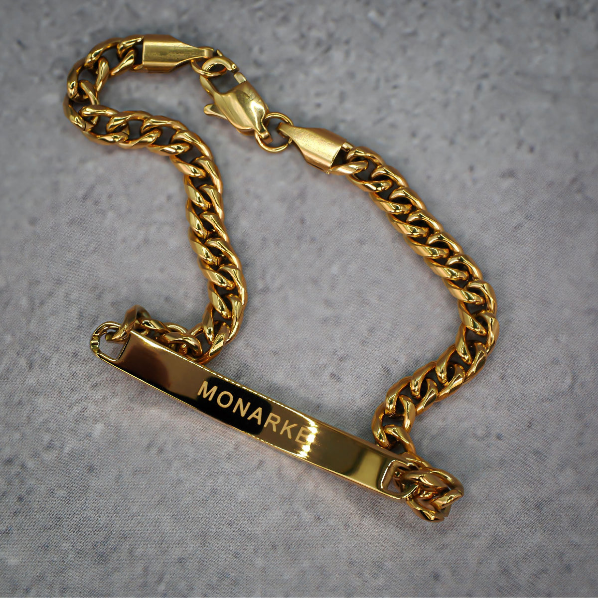 Gold chain bracelet with 'MONARKE' engraving on a grey background