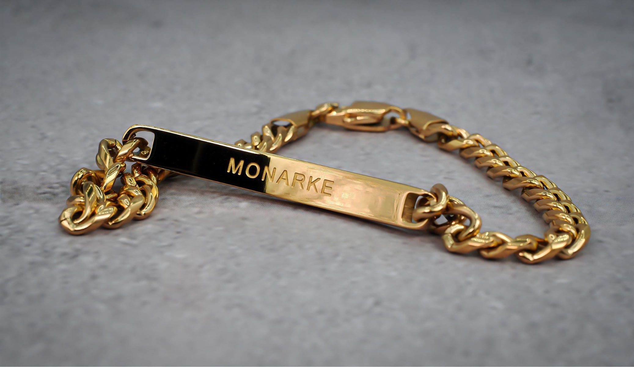 Gold chain bracelet with 'MONARKE' engraving on a grey background
