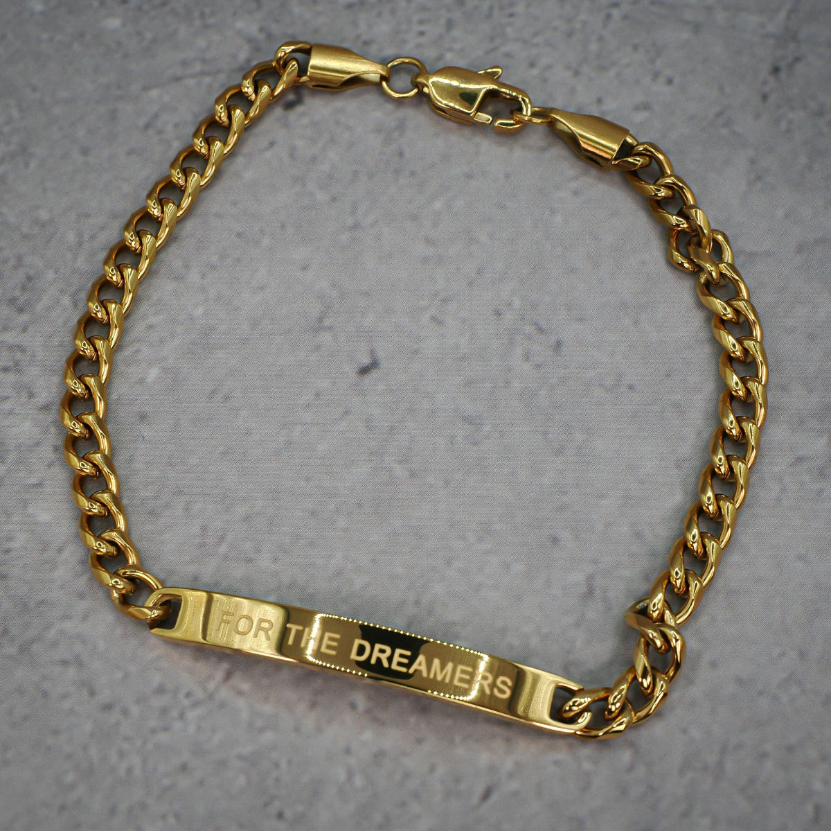Gold chain bracelet underside with 'For the Dreamers' tag on a grey background
