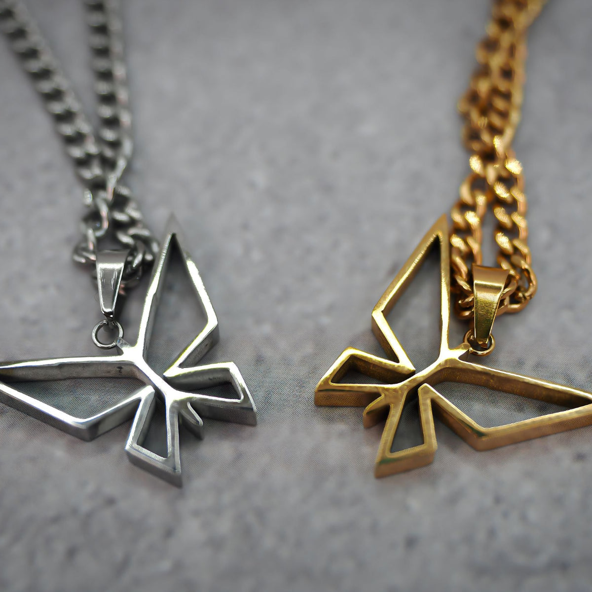 Two butterfly-shaped pendants, one silver and one gold, on a grey background.