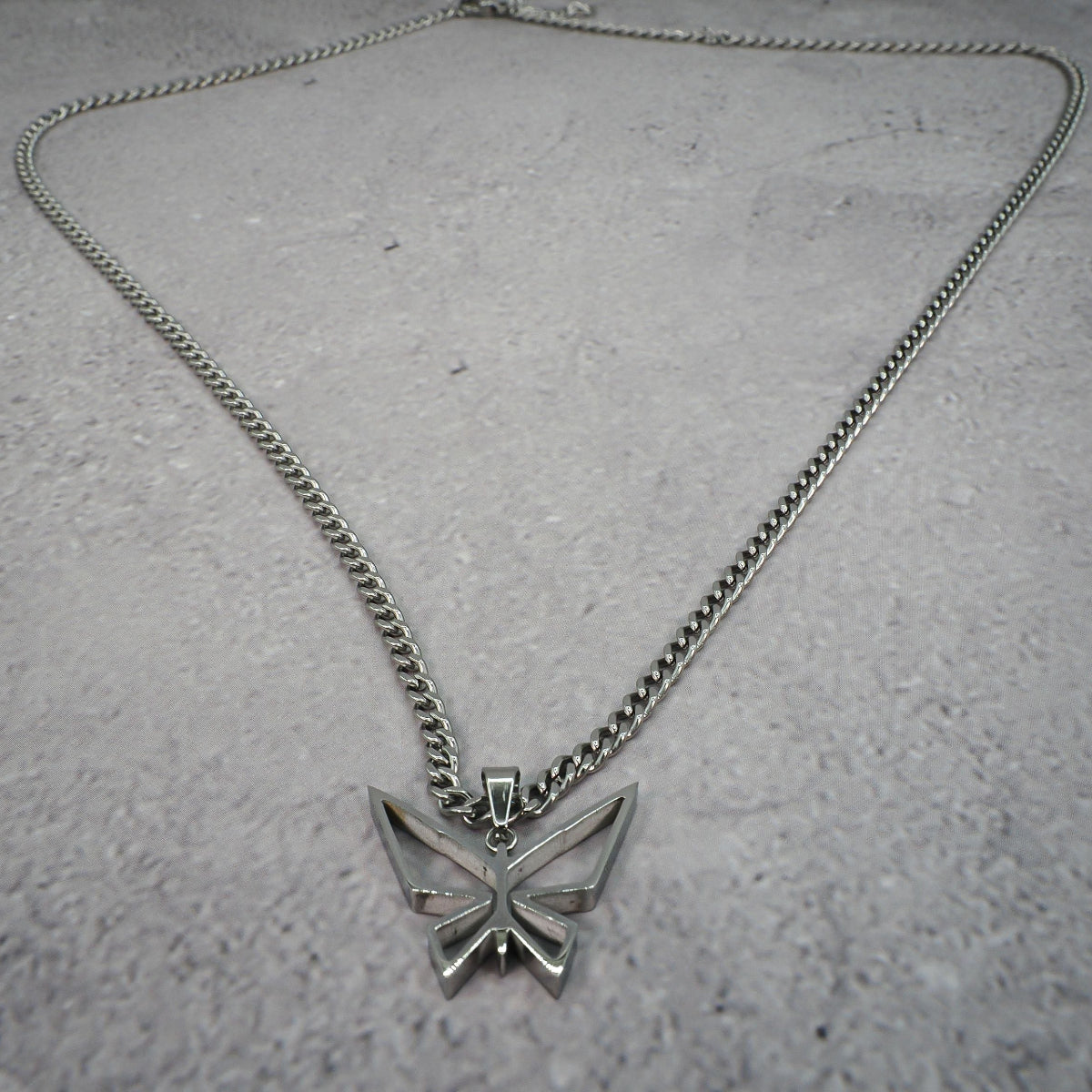 Silver butterfly pendant necklace on a textured grey counter.