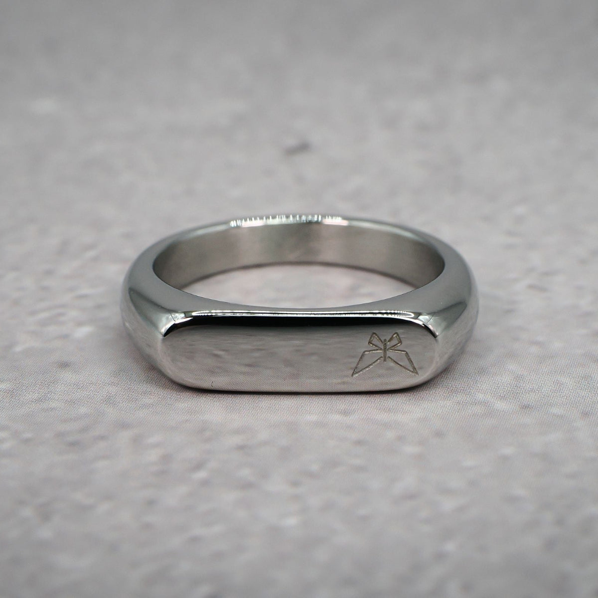 Front view of a silver ring with left aligned butterfly logo on a grey counter