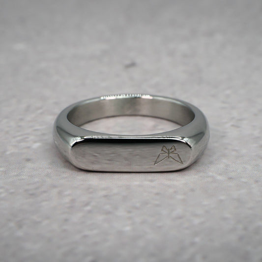 Front view of a silver ring with left aligned butterfly logo on a grey counter