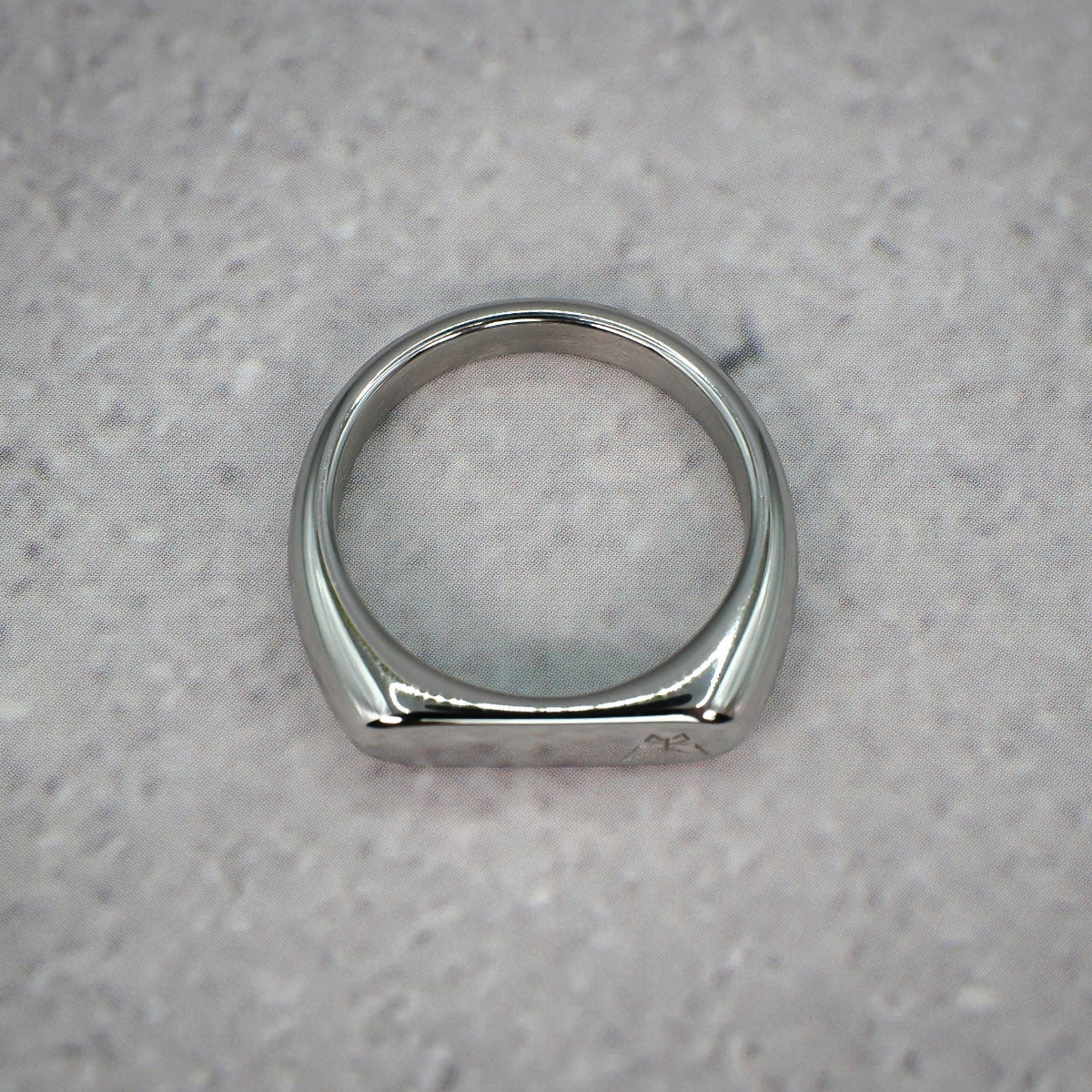 Top down view of a silver ring with left aligned butterfly logo on a grey counter