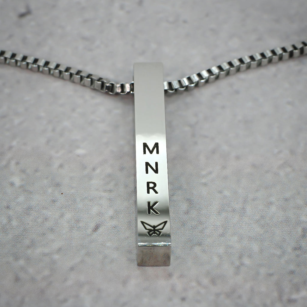 Silver bar pendant displaying 'MNRK' branding on a grey counter.