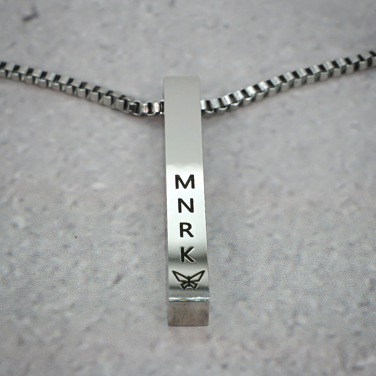 Silver bar pendant displaying 'MNRK' branding on a grey counter.