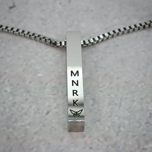 Silver bar pendant displaying 'MNRK' branding on a grey counter.